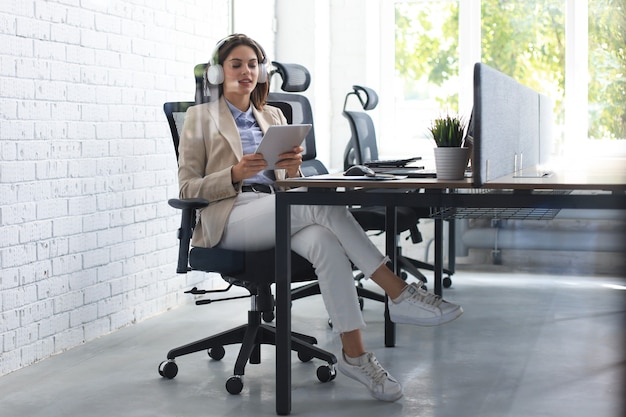 La foto attraverso il vetro di una bella donna d'affari caucasica sta lavorando utilizzando una tavoletta digitale mentre è seduta in un ufficio creativo.