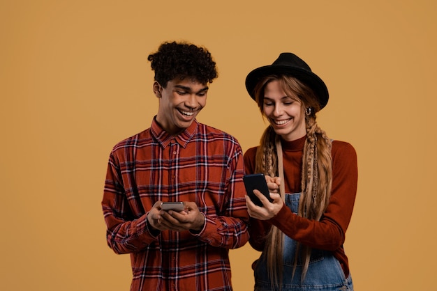 La foto degli agricoltori maschii e bianchi neri guarda i loro smartphone. L'uomo indossa una camicia a quadri, la donna indossa una tuta in denim e il cappello ha isolato lo sfondo di colore marrone.