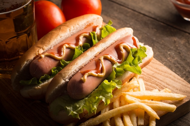 La foto del barbecue ha grigliato il hot dog con senape e ketchup gialli su fondo di legno. Panino hot dog con patate fritte e salse.