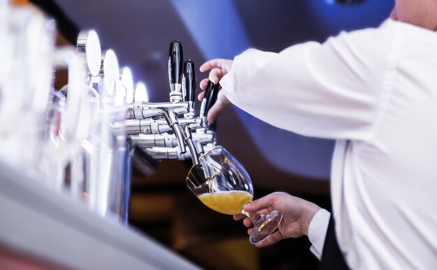 La foto del cameriere versa la birra in un bicchiere