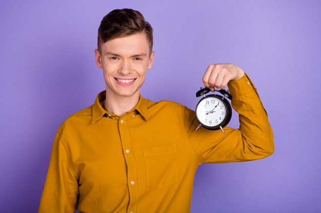 La foto del giovane ragazzo allegro di buon umore tiene la gestione della puntualità dell'orologio isolata su sfondo di colore viola