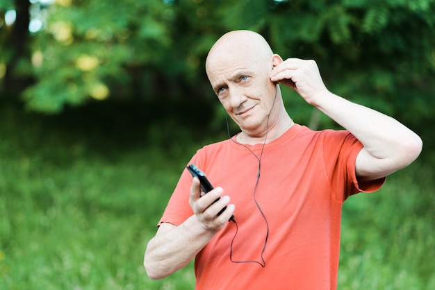 La foto del pensionato in pensione indossa le cuffie mentre ascolta la musica e cerca di udire nel parco.