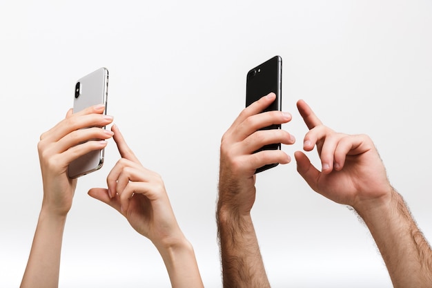 La foto del primo piano delle mani di un uomo e di una donna isolate sopra il muro bianco che tiene i telefoni cellulari scatta una foto.