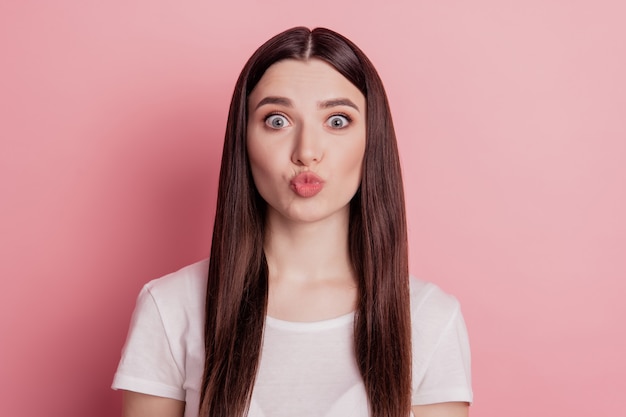 La foto del primo piano di una ragazza carina che invia baci d'aria indossa una maglietta bianca isolata con uno sfondo di colore rosa brillante