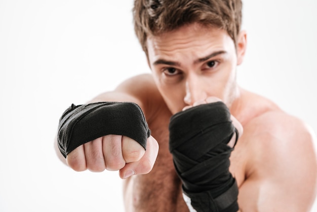 La foto del pugile serio del giovane fa gli esercizi di boxe sopra la parete bianca.