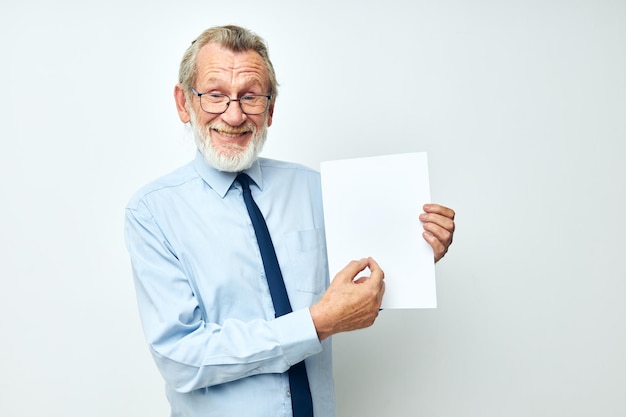 La foto del vecchio pensionato in una camicia con un foglio di carta del copyspace della cravatta ha isolato lo sfondo