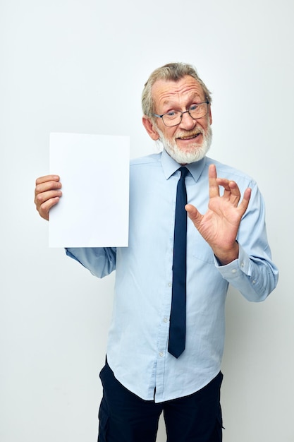 La foto del vecchio pensionato in una camicia con un foglio di carta del copyspace della cravatta ha isolato lo sfondo