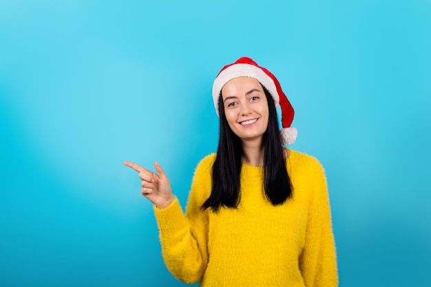 La foto dell'adorabile femmina positiva che indossa il cappello di Babbo Natale e il maglione giallo promuove lo shopping consigliato