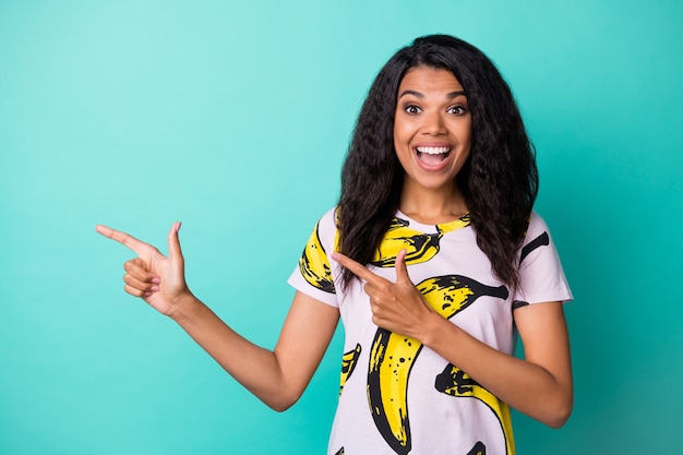 La foto della bocca aperta della giovane ragazza nera indica che lo spazio vuoto delle dita indossa una t-shirt con stampa di banana isolato sfondo di colore turchese