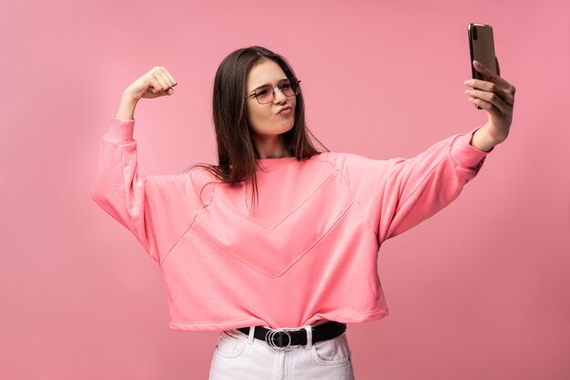 La foto della giovane donna attraente in vetri prende selfie e mostra i muscoli