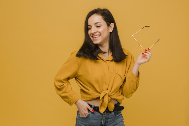 La foto della giovane donna tiene gli occhiali da sole e sembra così felice. Indossa maglietta gialla, sfondo di colore giallo isolato.