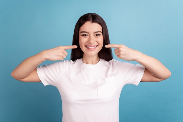 La foto della giovane ragazza carina indica la protezione della cavità igiene dei denti delle dita isolate su uno sfondo di colore blu.