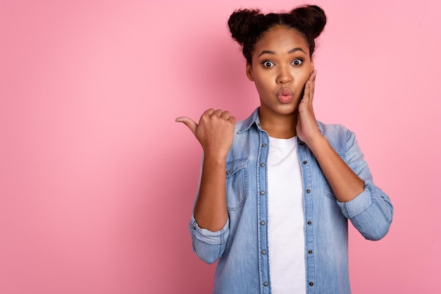 La foto della guancia tattile della giovane donna stupita indica lo spazio vuoto del dito pubblicizza isolato su sfondo di colore rosa