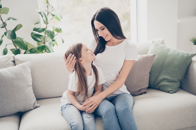 La foto della mamma amorevole si siede sul divano con la sua piccola figlia nella stanza della casa