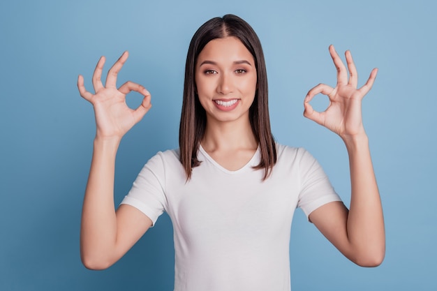 La foto della ragazza adorabile del promotore mostra segni ok guarda la telecamera in posa su sfondo blu