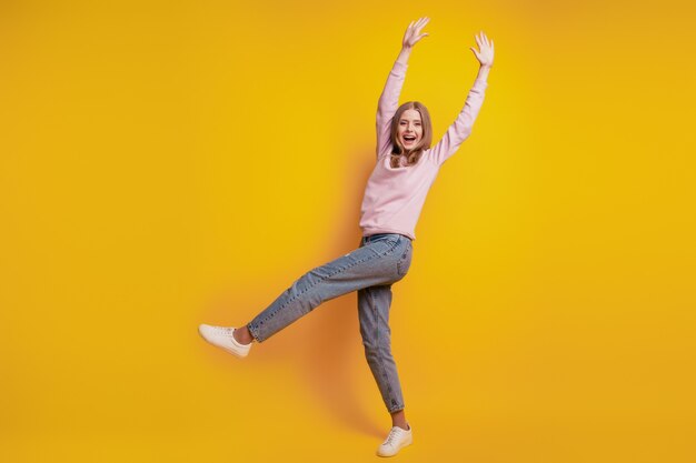 La foto della ragazza positiva sta con una gamba si diverte su sfondo giallo