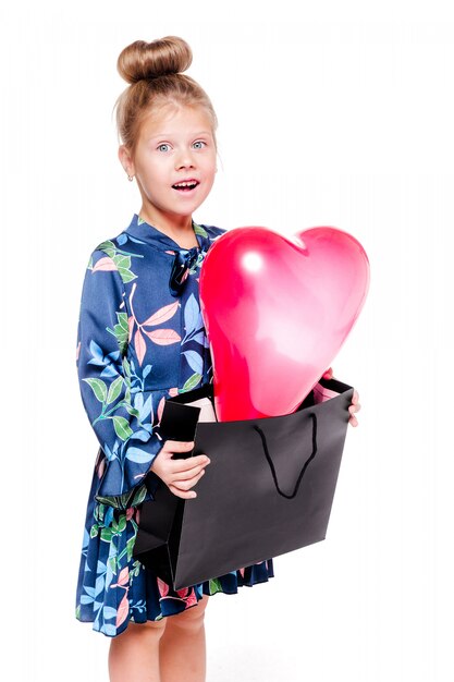 La foto della ragazzina alla moda in un abito floreale blu tiene una grande borsa con all'interno un palloncino a forma di cuore