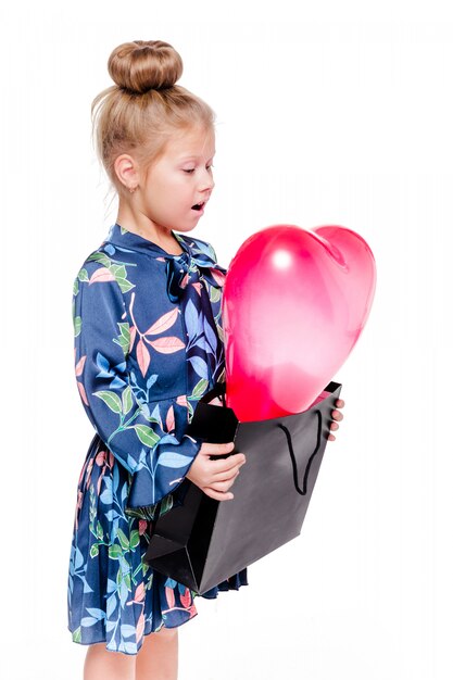 La foto della ragazzina alla moda in un abito floreale blu tiene una grande borsa con all'interno un palloncino a forma di cuore