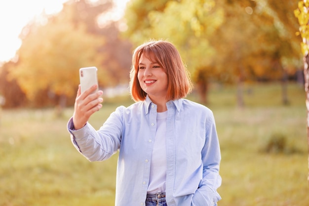 La foto della splendida signora acconciatura ondulata positiva fa selfie che registrano la strada del tramonto serale