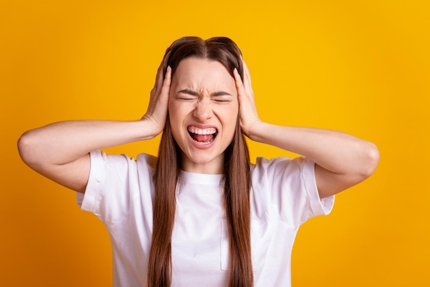 La foto delle braccia della giovane donna copre le orecchie irritata infastidita conflitto di urlo isolato su sfondo di colore giallo