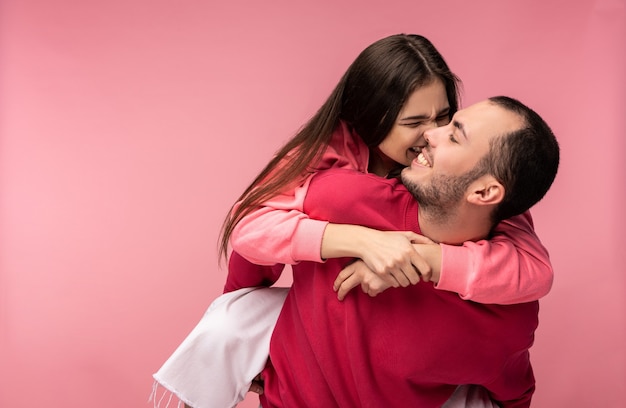 La foto delle coppie dolci si abbracciano e sorridono. Maschio e femmina sono innamorati. La donna cerca di mordere l'uomo. Isolato su sfondo rosa.