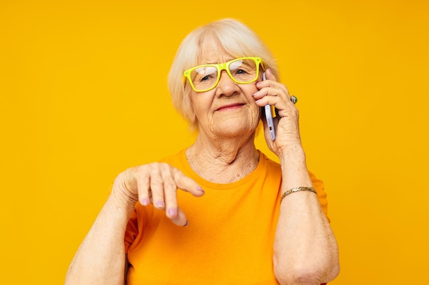 La foto dello stile di vita felice della vecchia signora in pensione in magliette gialle con il telefono ha isolato lo sfondo