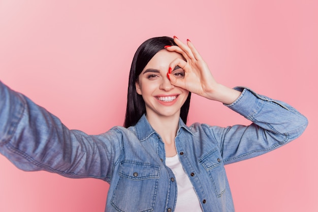 La foto di un'adorabile signora soddisfatta fa un sorriso raggiante di selfie e mostra un segno di approvazione isolato su uno sfondo di colore rosa