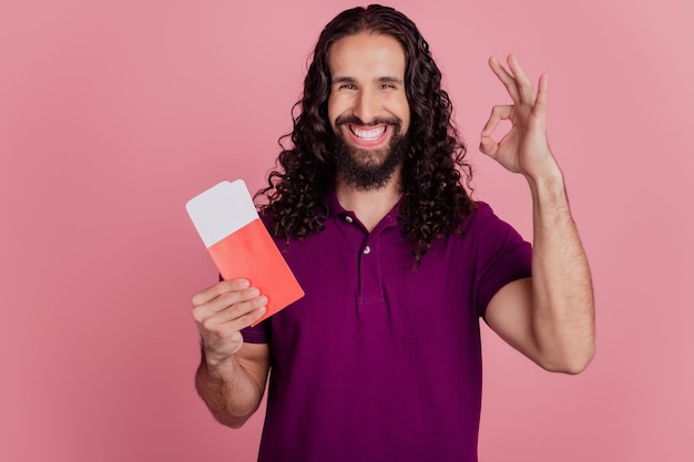 La foto di un promotore affidabile che tiene in mano biglietti a basso costo mostra un cartello ok indossa una maglietta viola isolata su uno sfondo di colore rosa