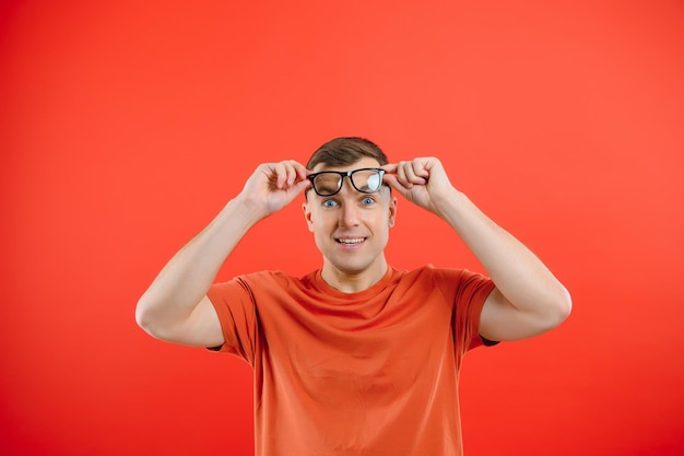 La foto di un ragazzo intelligente e intelligente sorridente indossa occhiali con una cattiva vista, un disadattato isolato su uno sfondo di colore rosso