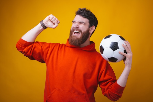 La foto di un tifoso di calcio o di calcio sta facendo il gesto del vincitore e sta tenendo una palla sullo spazio giallo.