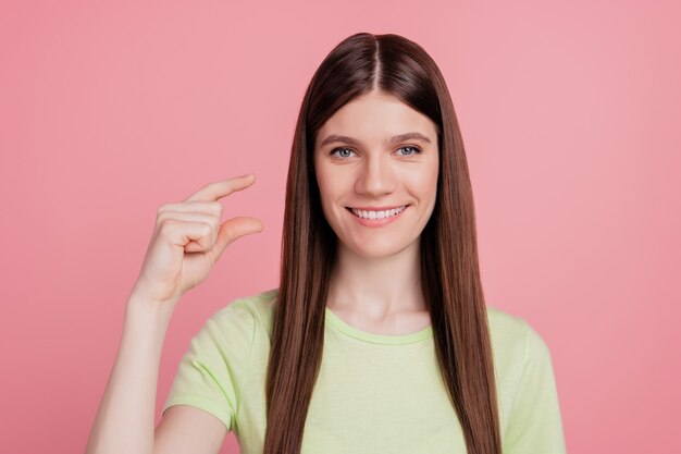 La foto di una giovane donna allegra con un sorriso felice mostra le dita piccole misure di dimensioni minuscole isolate su uno sfondo di colore rosa