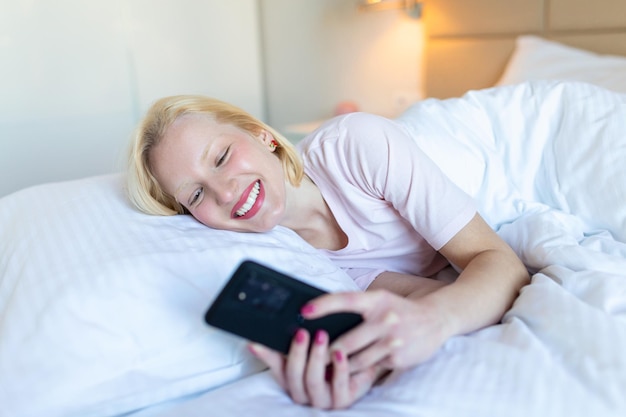 La foto di una giovane donna sorridente ha una videochiamata di notte mentre è sdraiata su un letto nella sua camera da letto