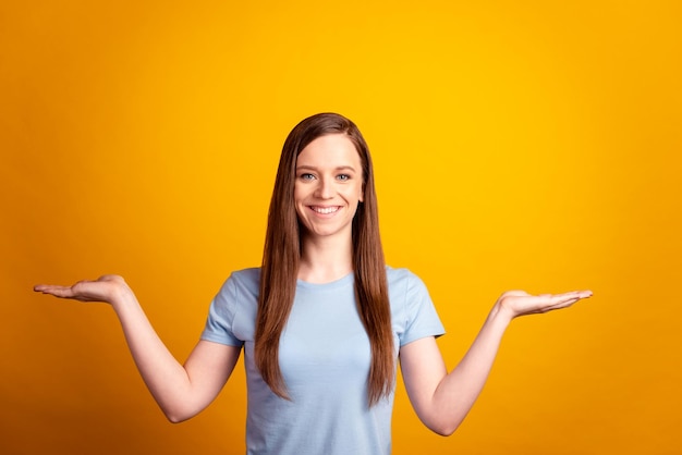 La foto di una giovane ragazza allegra si tiene per mano la promozione della soluzione pubblicitaria isolata su uno sfondo di colore giallo