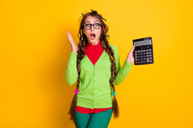 La foto di una ragazza geek con una pettinatura disordinata tiene la calcolatrice stupita e ha isolato uno sfondo di colore brillante