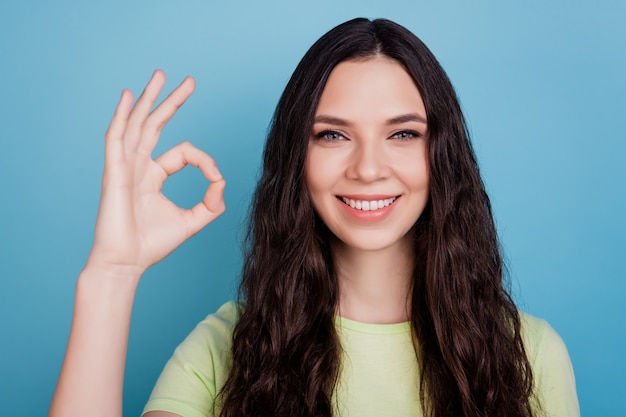 La foto di una ragazza positiva del promotore affidabile dimostra un gesto ok su sfondo blu