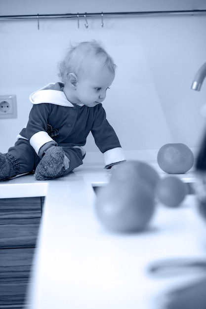 La foto monocromatica del piccolo bambino biondo in cucina si siede su un tavolo