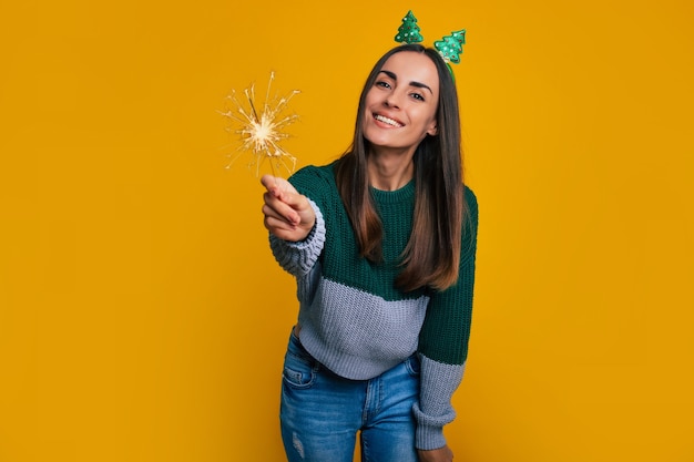 La foto ravvicinata di una bella donna alla moda eccitata in un maglione natalizio casual con stelle filanti in mano è in posa isolata su sfondo giallo e si diverte