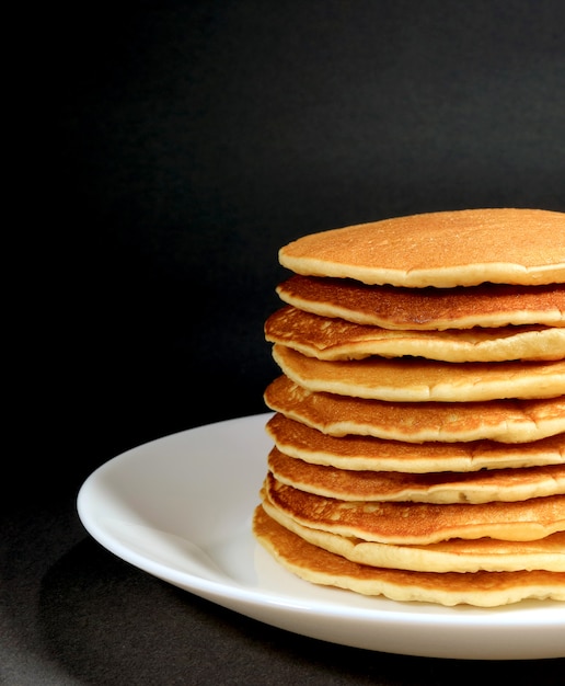 La foto verticale della pila normale casalinga fresca dei pancake è servito sul piatto bianco su fondo nero