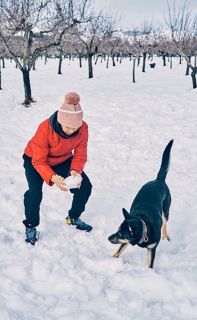 La foto verticale di una ragazza caucasica molto calda e con indosso un cappello gioca nella neve con il suo cane.