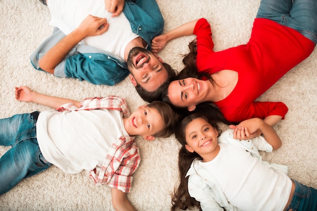 La foto vista dall'alto di una giovane e bella famiglia felice sdraiata sul pavimento si diverte e sorride mentre guarda la fotocamera