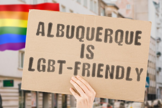 La frase "Albuquerque è LGBT-Friendly" su uno striscione in mano da uomo con una bandiera LGBT sfocata sullo sfondo. Relazioni umane. diverso. Diversi. libertà. Sessualità. Questioni sociali. Società