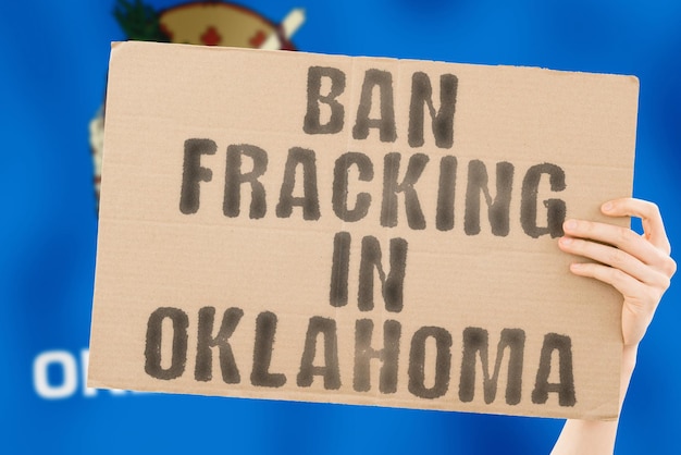 La frase Ban fracking in Oklahoma su uno striscione in mano maschile con la bandiera offuscata dell'Oklahoma sullo sfondo Estratto di natura Tubo di arresto Trapano energetico Potenza grezza Combustibile Crisi fossile