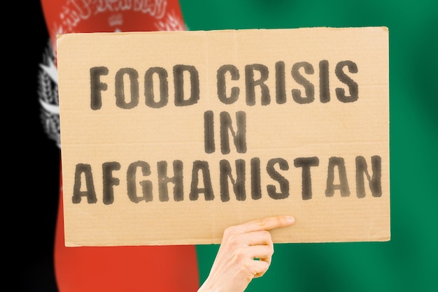 La frase Crisi alimentare in Afghanistan è su uno striscione nelle mani degli uomini con una bandiera afgana sfocata sullo sfondo Crisi Finanza Vita Nutrizione Pane Disastro Crollo Problema sociale Problema
