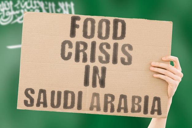 La frase Crisi alimentare in Arabia Saudita è su uno striscione nelle mani degli uomini con una bandiera sfocata dell'Arabia Saudita sullo sfondo Crisi Finanza Vita Nutrizione Pane Disastro Crollo Problema sociale