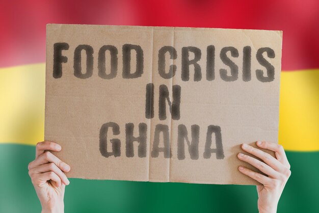 La frase Crisi alimentare in Ghana è su uno striscione nelle mani degli uomini con una bandiera ghanese sfocata sullo sfondo Crisi Finanza Vita Nutrizione Pane Disastro Crollo Problema sociale