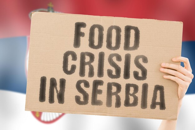 La frase Crisi alimentare in Serbia è su uno striscione nelle mani degli uomini con una bandiera serba sfocata sullo sfondo Crisi Finanza Vita Nutrizione Pane Disastro Crollo Problema sociale