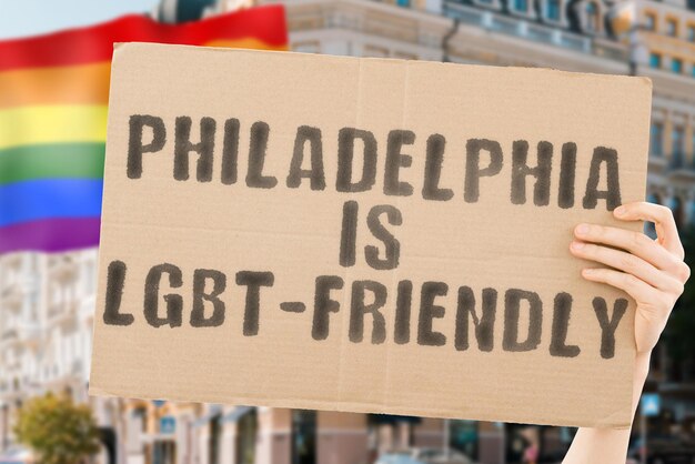 La frase "Philadelphia is LGBT-Friendly" su uno striscione in mano da uomo con la bandiera LGBT sfocata sullo sfondo. Relazioni umane. diverso. Diversi. libertà. Sessualità. Questioni sociali. Società