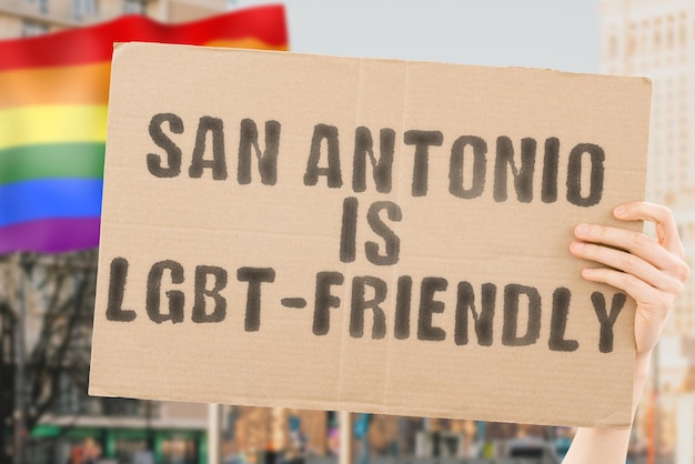 La frase "San Antonio è LGBT-Friendly" su uno striscione in mano maschile con bandiera LGBT sfocata sullo sfondo. Relazioni umane. diverso. Diversi. libertà. Sessualità. Questioni sociali. Società