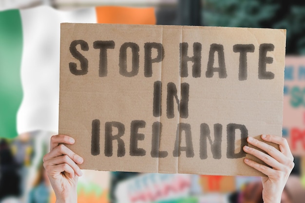 La frase Stop all'odio in Irlanda su uno striscione in mano agli uomini con la bandiera irlandese sfocata sullo sfondo Gay Diritti umani Uguaglianza Questioni sociali Società Problema Conflitto