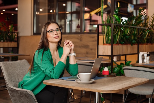 La freelance femminile sta lavorando con un laptop all'interno della caffetteria o dell'area di coworking